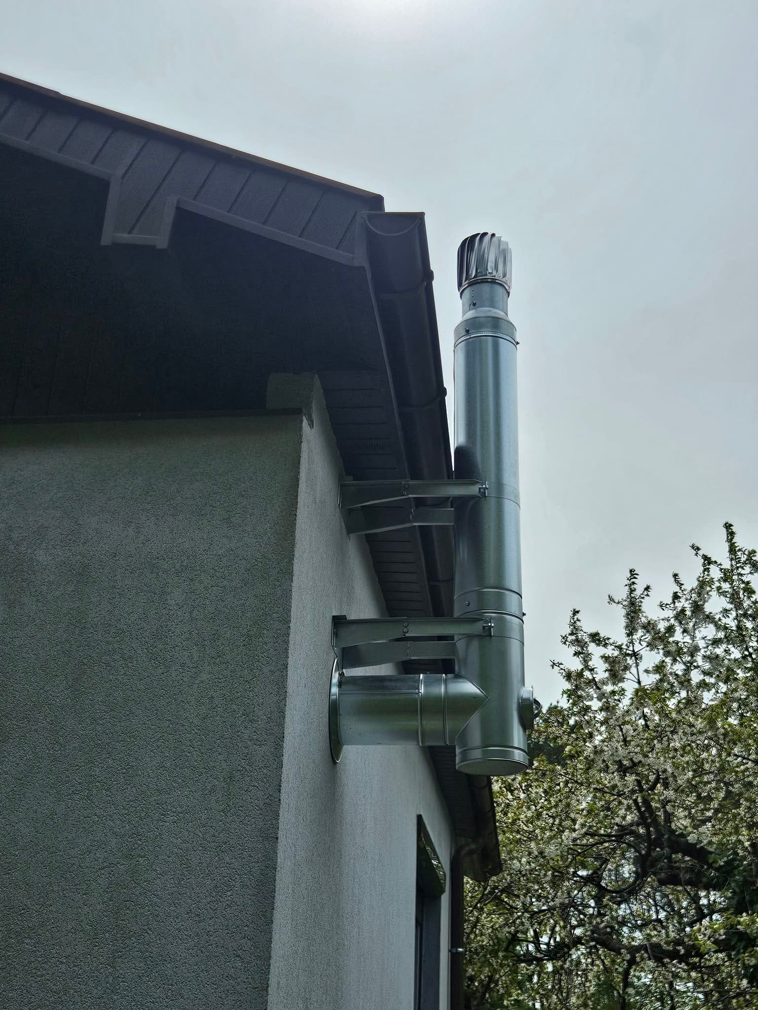 Zewnętrzny komin stalowy z nasadą obrotową na szarej elewacji